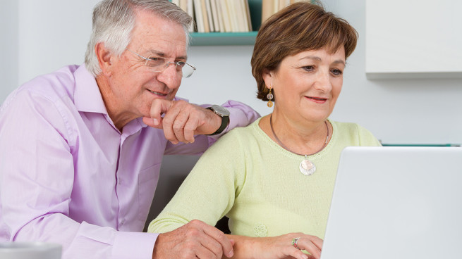 an older gentlemen and his wife smile while using a computer
